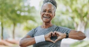 menopausal older woman exercising outdoors for heart health with hands over heart in heart shape